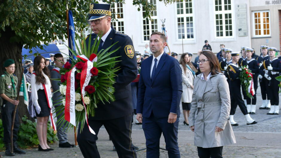 zastępca PMG Piotra Borawski składa wieniec trzymany przez strażnika miejskiego