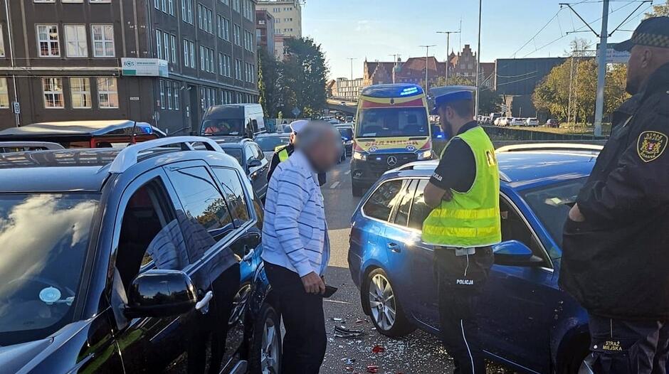 policjant rozmawia z mezczyzna, w tle stoja inne auta i karetka