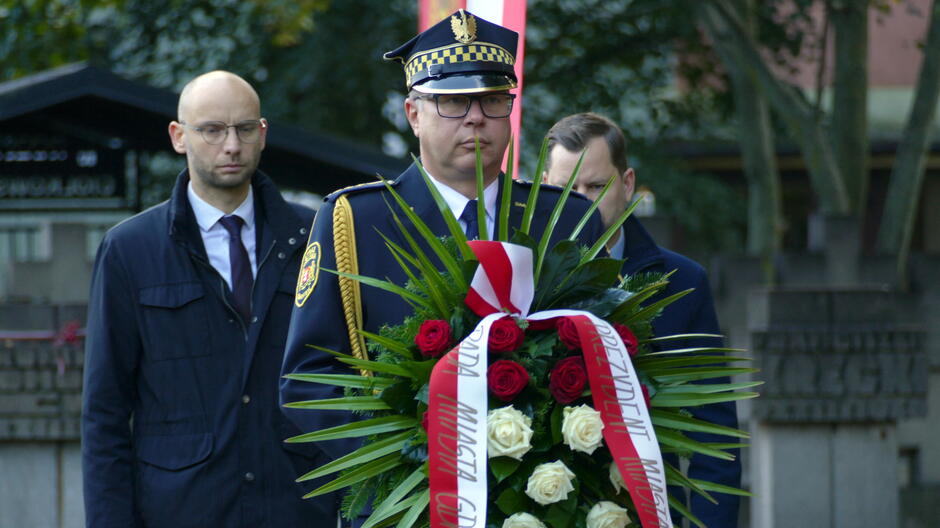 strażnik niesie wieniec za nim idzie Piotr Kryszewski