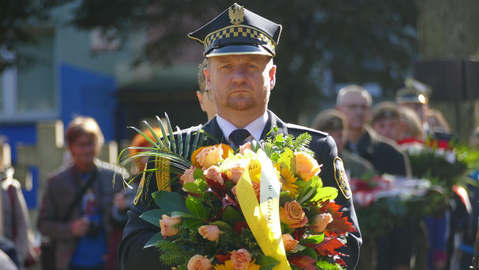 strażnik niesie wieniec. w tle uczestnicy uroczystości