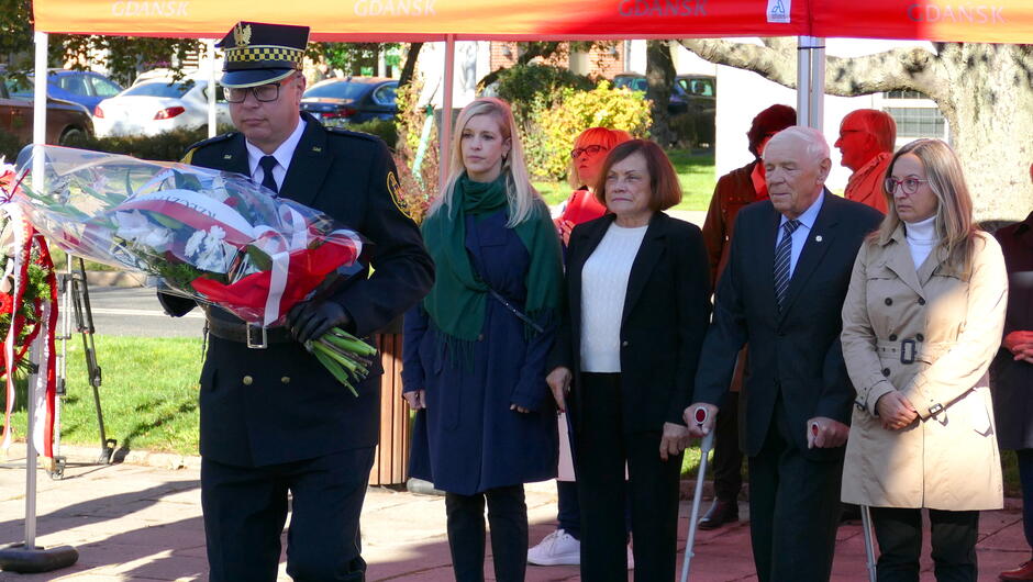 strażnik z wiązanką kwiatów, w tle uczestnicy wydarzenia