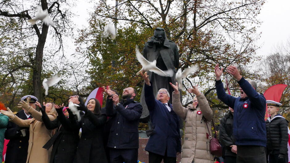 uczestnicy wypuszczaja białe gołębie, w tle pomnik