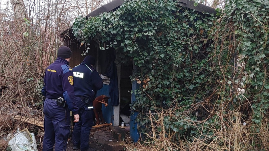 Strażnik miejski i policjant zaglądają do szałasu w poszukiwaniu osób w kryzysie bezdomności. 