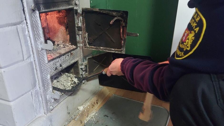 piec kaflowy obok niego strażniczka sprawdzająca zawartość popielnika