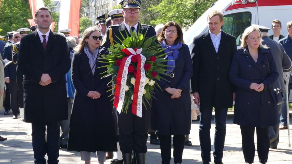 Stoi strażnik miejski z wieńcem, a za nim delegacja przedstawicieli władz miasta Gdańska z prezydent Aleksandrą Dulkiewicz na czele.