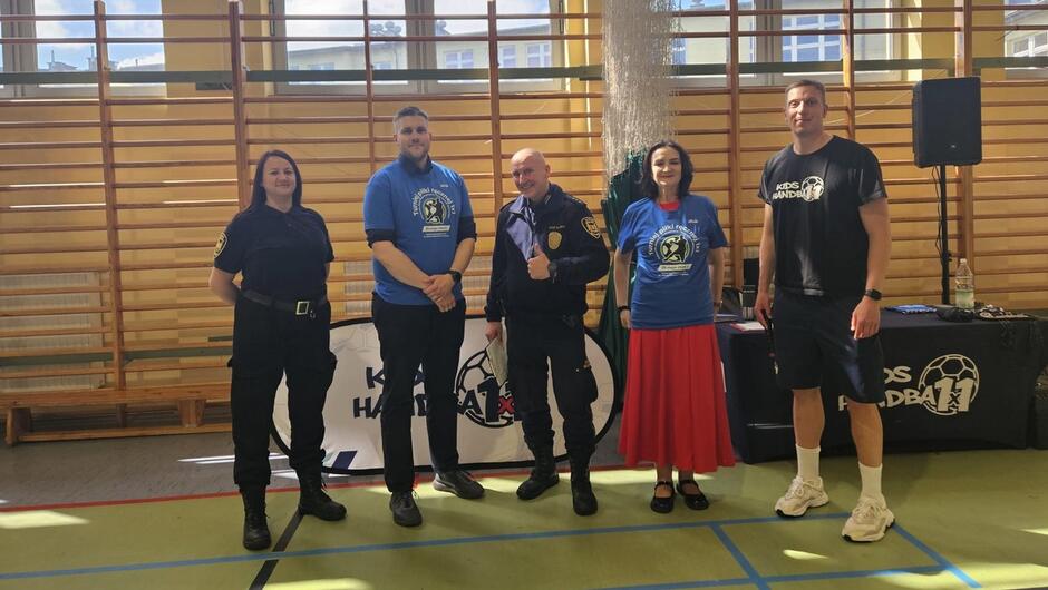 organizatorzy i trenerzy i strażnik miejski pozują do zdjęcia na tle drabinek w tle okno