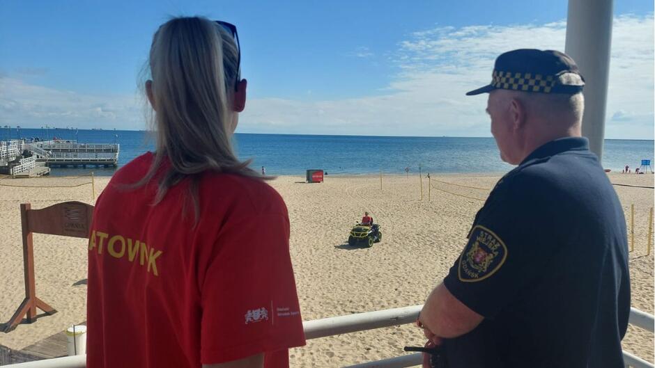 Ratowniczka i strażnik miejski stoją na plaży i patrzą w kierunku morza.