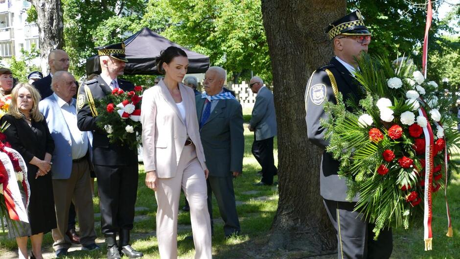 Strażnik miejski niesie wieniec, za nim wojewoda pomorska Barbara Rutkiewicz.