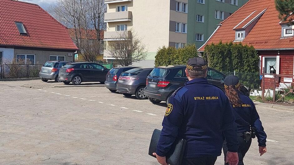 strażnicy idą ulicą i oglądają nieruchomości na parkingu zaparkowane samochody