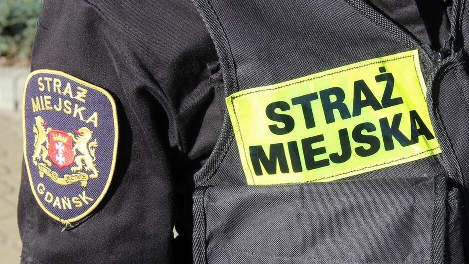 fragment umundurowania strażnika z emblematem straży miejskiej w gdańsku i odblaskowym, zielonym napisem straż miejska