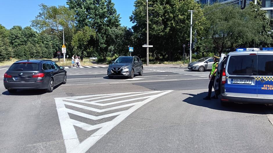 dwa auta na skrzyzowaniu, obok skrzyzowania radiowoz straznikow