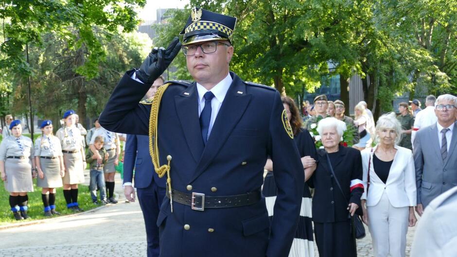 Strażnik miejski salutuje, za nim delegacja władz miasta i kombatantów.