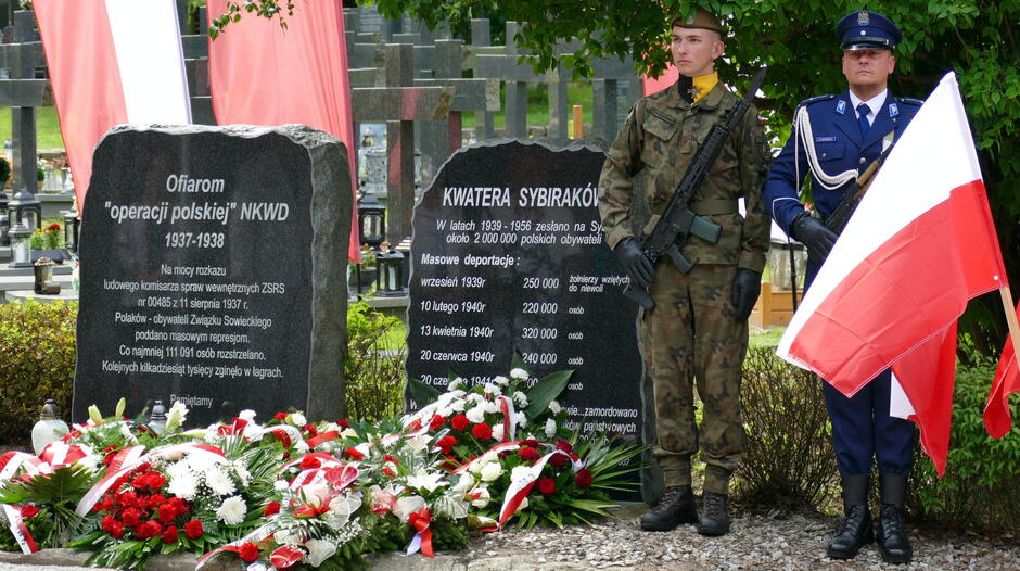 pomnik przy którym stoi warta honorowa złożona z żołnierza i policjanta