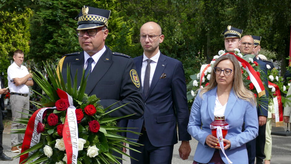 strażnik idzie z wieńcem, za nim przedstawiciele władz miasta