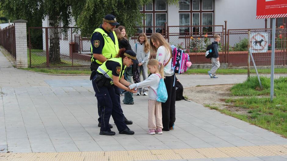 Strażnicy miejscy rozdają dzieciom odblaski.