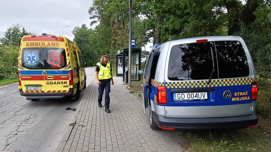 po lewej karetka, a po prawej radiowoz strażników, pomiędzy strażniczka
