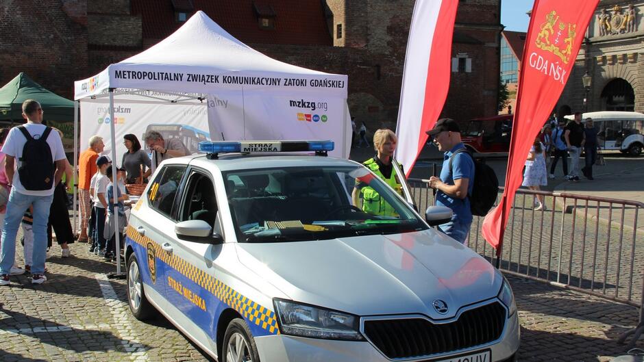 strażniczka rozmawia z mężczyzną stoją przy radiowozie za nimi stoi biały namiot z napisem mzkg.pl