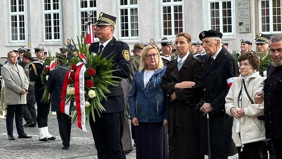 strażnik trzyma wieniec obok uczestnicy