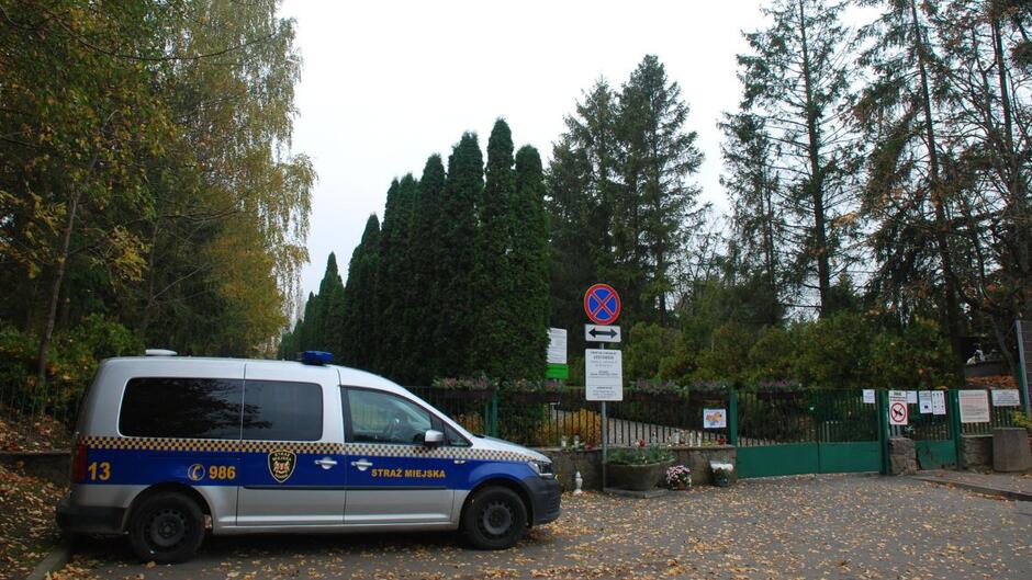 Radiowóz Straży Miejskiej stoi przed cmentarzem.