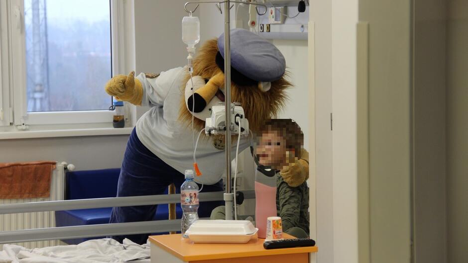 strażnik w stroju lwa pozuje do zdjęcia z chłopcem na szpitalnym łóżku