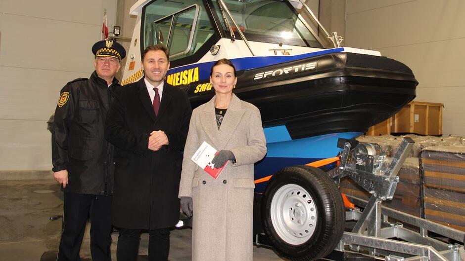 Od prawej wojewoda pomorska Barbara Rutkiewicz, wiceprezydent Gdańska Piotr Borawski oraz komendant Straży Miejskiej w Gdańsku Leszek Walczak na tle łodzi motorowej w hangarze.