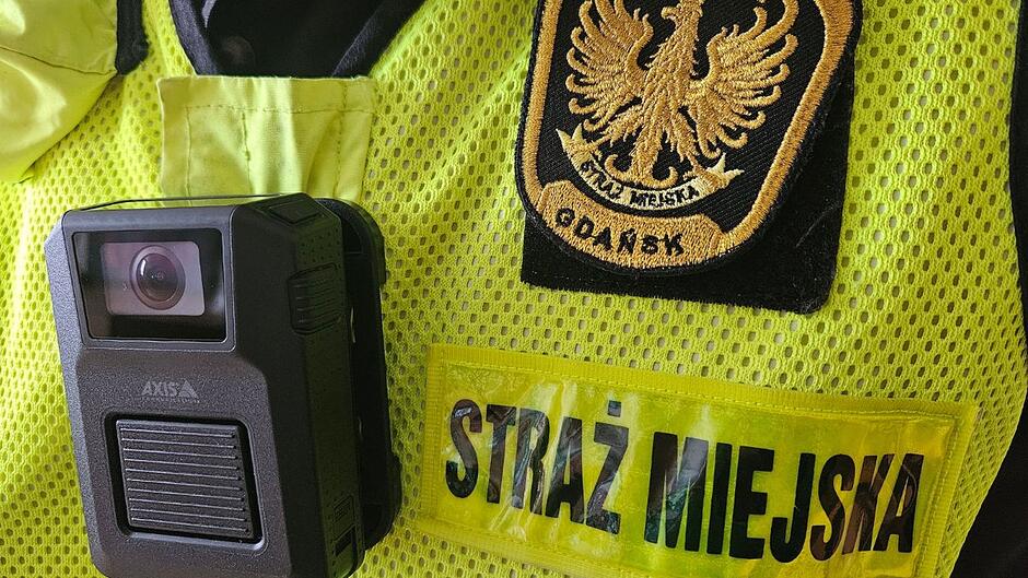 Kamerka nasobna na kamizelce strażnika miejskiego. Obok napis Straż Miejska, powyżej napis Gdańsk i orzełek.