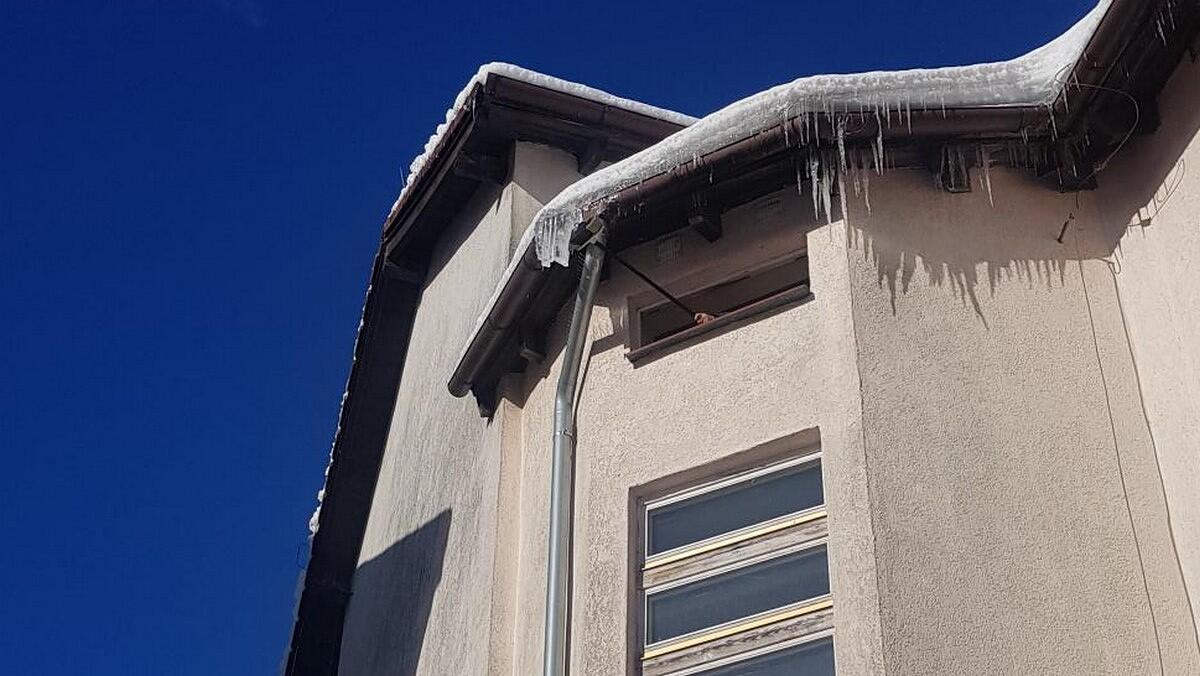 fragment bloku mieszkalnego. w oknie pod dachem widać rękę, która trzyma miotłę i zrzuca sople z pod dachu.