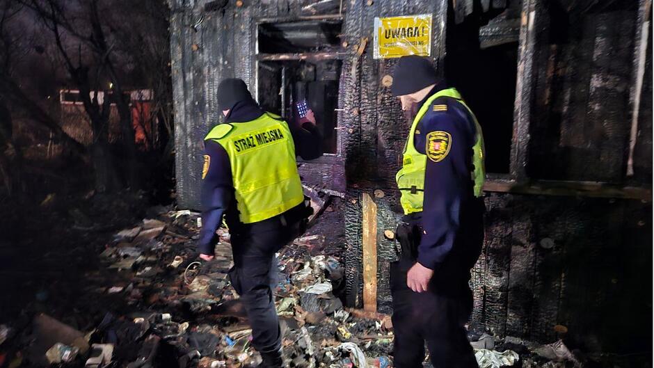 Dwóch strażników miejskich poszukuje osób w kryzysie bezdomności w zrujnowanym domu. 
