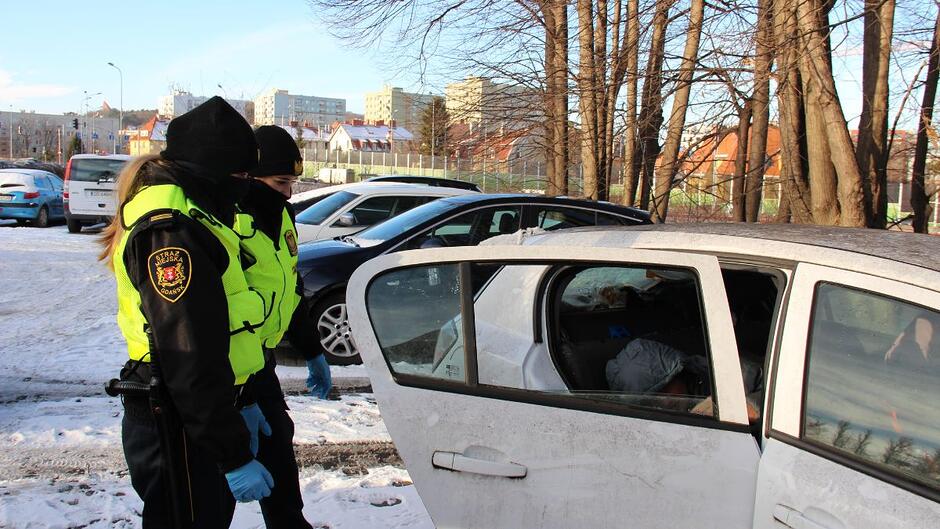 Dwie strażniczki miejskie stoją przed otwartymi drzwiami samochodu, w którym znajduje się osoba w kryzysie bezdomności.