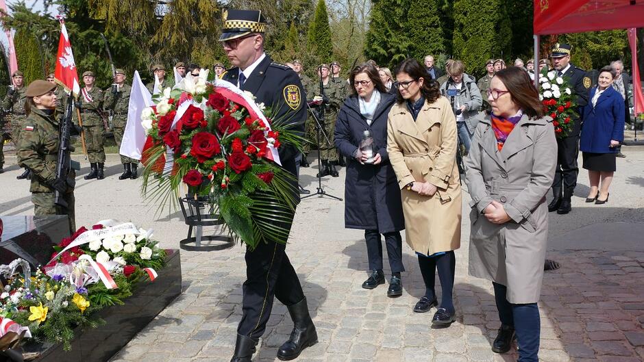 Strażnik niesie wieniec, za nim delegacja władz miasta z Aleksandrą Dulkiewicz, Prezydent Miasta Gdańska na czele.