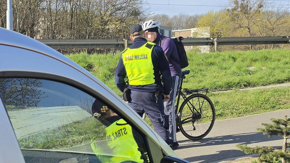 Kontrola rowerzysty na skrzyżowaniu z wyznaczonym przejazdem rowerowym. Strażnicy miejscy sprawdzają przestrzeganie przepisów ruchu drogowego przez użytkowników rowerów.