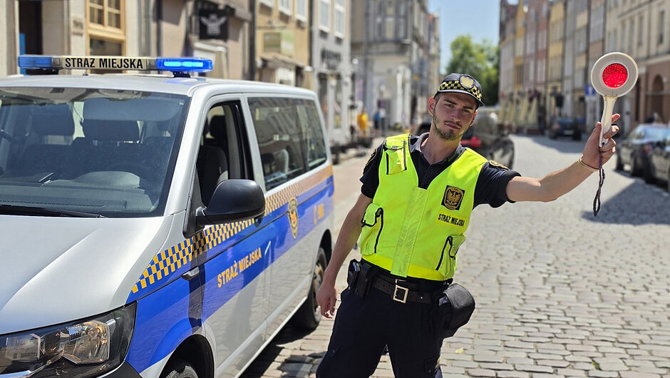 Na trzecim zdjęciu widoczny jest pojazd Straży Miejskiej oraz funkcjonariusz kierujący ruchem przy użyciu tarczy do zatrzymywania pojazdów. Sytuacja wskazuje na prowadzenie zabezpieczenia organizacji ruchu i kontrolę dostępu do strefy objętej czasowymi ograniczeniami.