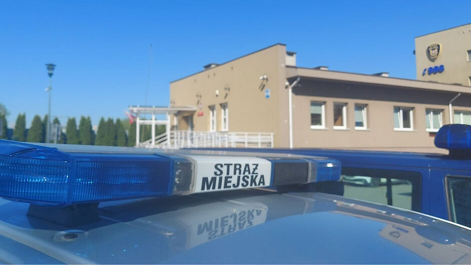 Napis Straż Miejska na dachu radiowozu. W tle siedziba Straży Miejskiej w Gdańsku.