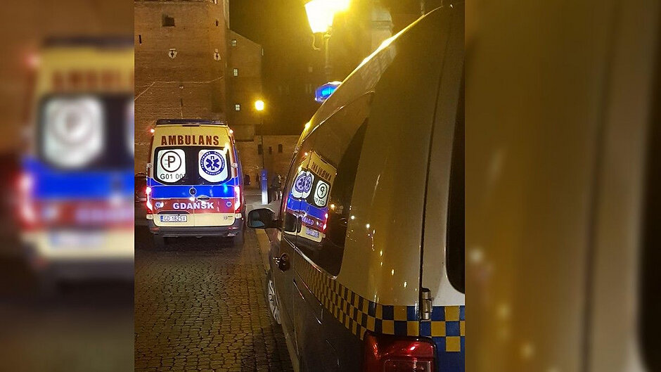 Na pierwszym planie bok radiowozu straży miejskiej, a przed nim karetka pogotowia ratunkowego.