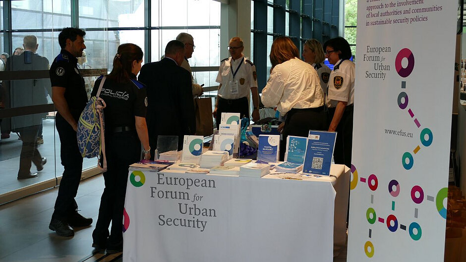 Na pierwszym planie stoisko z broszurami informacyjnymi EFUS. Za nim stoją pracownicy Straży Miejskiej w Gdańsku rejestrujący uczestników konferencji z europejskich policji municypalnych. 