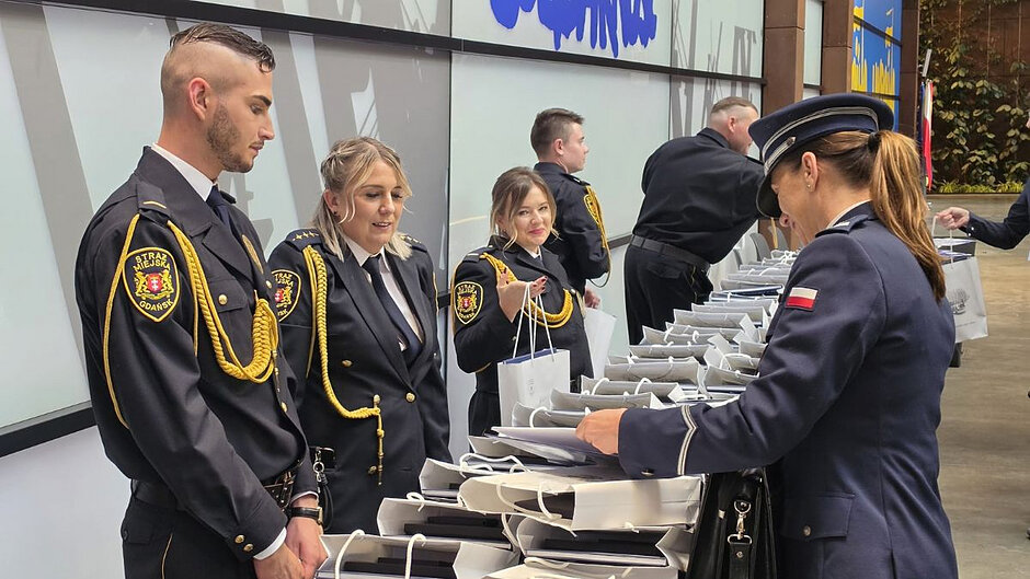 Strażnicy miejscy wręczają pamiątkowe zestawy upominków gościom jubileuszu Straży Miejskiej w Gdańsku.