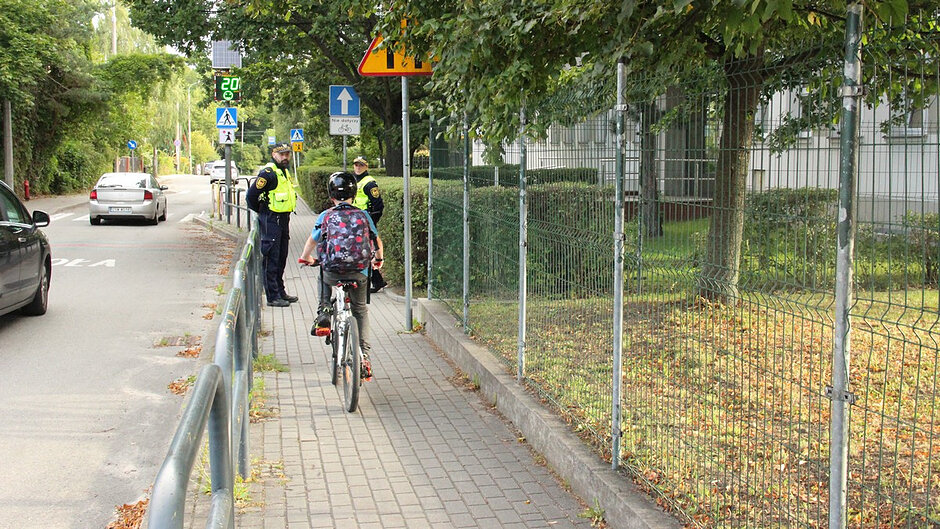 Na drugim zdjęciu widać młodego rowerzystę poruszającego się drogą dla rowerów w pobliżu szkoły. Strażnicy rozmawiają z uczniami o obowiązkowym wyposażeniu roweru, zasadach jazdy oraz odpowiedzialnym korzystaniu z infrastruktury rowerowej.
