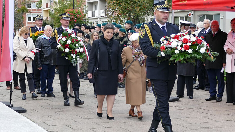 Strażnik miejski niesie wieniec, za nim reprezentacja wojewody pomorskiej, kolejny strażnik z kwiatami i kolejna reprezentacja.