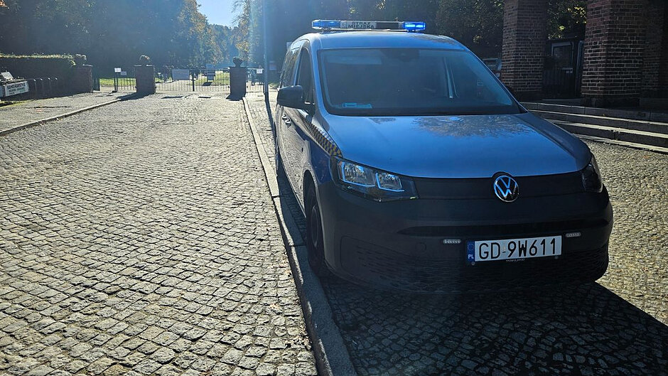 Radiowóz straży miejskiej stoi przed bramą Cmentarza Srebrzysko. 
