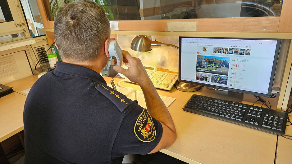 Strażnik miejski siedzi tyłem do fotografa i rozmawia przez telefon.