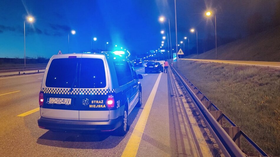 radiowóz z włączonymi sygnałami pojazdu uprzywilejowanego na obwodnicy w tle samochód osobowy