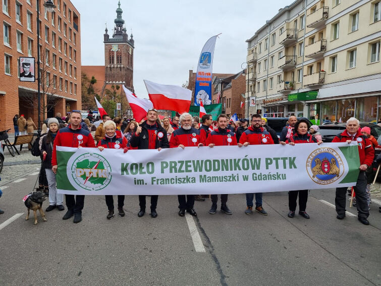 Zdjęcie przedstawia grupke przewodników trzymających baner z nazwą i logo oddziału gdańskiego pttka na ul. Rajskiej